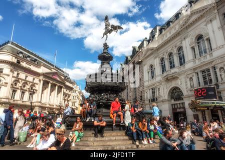 Touristen sahen, wie sie auf den Stufen des Shaftesbury Memorial Fountain und der Statue des griechischen gottes Anteros im Piccadilly Circus, London, saßen. Stockfoto