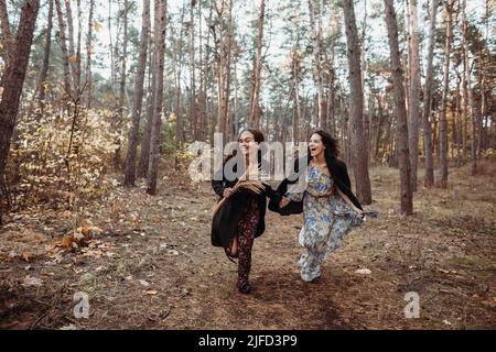 Zwei junge Frauen, die Spaß haben, mit Händen durch den Herbstwald zu laufen Stockfoto