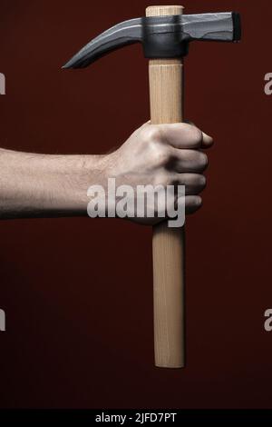 Hand des Mannes hält Hammer auf rotem Hintergrund Stockfoto