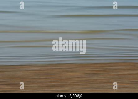 Bewegungsunschärfen von Lichtwellen an einem Kiesstrand, die ein weiches und glattes Bild erzeugen. Stockfoto