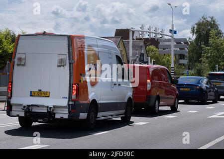 Lieferwagen der niederländischen Post 'PostNL' wartet vor einer Ampel hinter anderen Autos. Die Bremsleuchten sind sichtbar. Kurierfirma Stockfoto