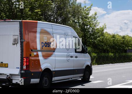 Lieferwagen der niederländischen Postfirma 'PostNL' fährt auf einer Asphaltstraße, um ein Paket an den nächsten Kunden zu liefern. Kurierfirma Stockfoto