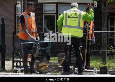 Mitarbeiter des niederländischen Telefonunternehmens KPN arbeiten mit einem tragbaren Schwingungsstamper, um nach dem Verlegen von Kabeln den Sand abzuschleifen. Straßenarbeiten Stockfoto