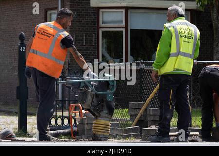 Mitarbeiter des niederländischen Telefonunternehmens KPN arbeiten mit einem tragbaren Schwingungsstamper, um nach dem Verlegen von Kabeln den Sand abzuschleifen. Straßenarbeiten Stockfoto