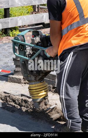 Mitarbeiter der niederländischen Telefongesellschaft KPN arbeitet mit einem tragbaren Schwingungsstamper, um nach dem Verlegen von Kabeln den Sand abzuschleifen. Straßenarbeiten Stockfoto
