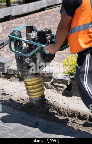 Mitarbeiter der niederländischen Telefongesellschaft KPN arbeitet mit einem tragbaren Schwingungsstamper, um nach dem Verlegen von Kabeln den Sand abzuschleifen. Straßenarbeiten Stockfoto
