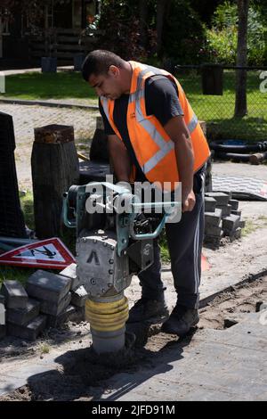 Mitarbeiter der niederländischen Telefongesellschaft KPN arbeitet mit einem tragbaren Schwingungsstamper, um nach dem Verlegen von Kabeln den Sand abzuschleifen. Straßenarbeiten Stockfoto
