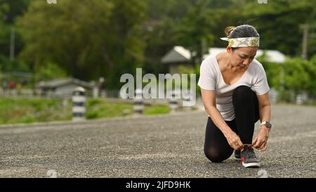 Frau mittleren Alters, die Schnürsenkel bindet und sich zum Joggen im Freien bereit macht. Gesundes Lifestyle-Konzept Stockfoto