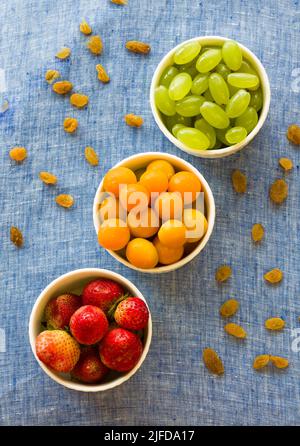 Obstschale mit gemischter Mischung aus frischen, saftigen Cape Stachelbeeren, Trauben und Erdbeeren, isoliert auf dunklem rustikalem Hintergrund. Backlit, Nahaufnahme, veganes Konzept Stockfoto