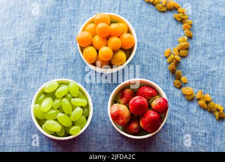 Obstschale mit gemischter Mischung aus frischen, saftigen Cape Stachelbeeren, Trauben und Erdbeeren, isoliert auf dunklem rustikalem Hintergrund. Backlit, Nahaufnahme, veganes Konzept Stockfoto