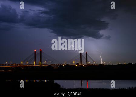 Dramatische nächtliche Aufnahme von Blitzeinschlägen in der Nähe einer Kabelbrücke über den Fluss Waal in den Niederlanden Stockfoto