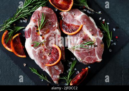 Rohe Schweinesteaks mit Rosmarin und Orange auf einem Steinbrett mariniert. Kochen von Fleischsteaks. Stockfoto