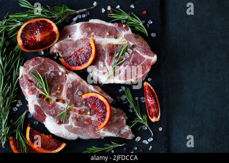 Rohe Schweinesteaks mit Rosmarin und Orange auf einem Steinbrett mariniert. Kochen von Fleischsteaks. Stockfoto