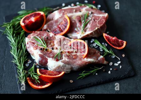 Rohe Schweinesteaks mit Rosmarin und Orange auf einem Steinbrett mariniert. Kochen von Fleischsteaks. Stockfoto