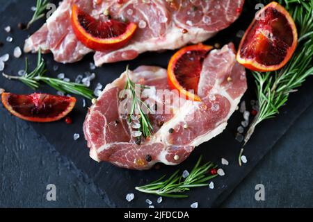 Rohe Schweinesteaks mit Rosmarin und Orange auf einem Steinbrett mariniert. Kochen von Fleischsteaks. Stockfoto