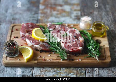 Rohe Schweinesteaks mit Rosmarin, grobem Salz und Zitrone. Frisches Schweinefleisch. Nackensteak. Bio-Fleisch Keto Pegan. Paleo-Diät. Stockfoto