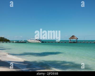 Ein hölzerner Pier an einem paradiesisch leeren Strand mit einer großen Yacht, die in der Nähe geparkt ist Stockfoto