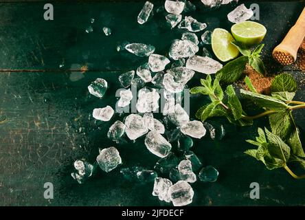 Draufsicht auf die Zutaten für den Mojito-Cocktail, einschließlich einer Menge Eiswürfel auf einem schäbigen Tisch mit grünen Minzblättern und frischen Limettenscheiben Stockfoto