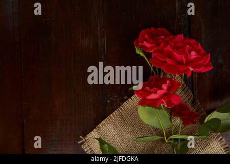 Rote Rosen Hintergrund auf Sacking auf Holzhintergrund. Geschenk, Geschenke. Speicherplatz kopieren. Stockfoto