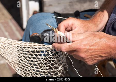 Enkhuizen, Niederlande. Juni 2022. Die Hände eines Fischers, der Fischernetze mit Nadel und Faden repariert. Hochwertige Fotos. Nahaufnahme. Stockfoto