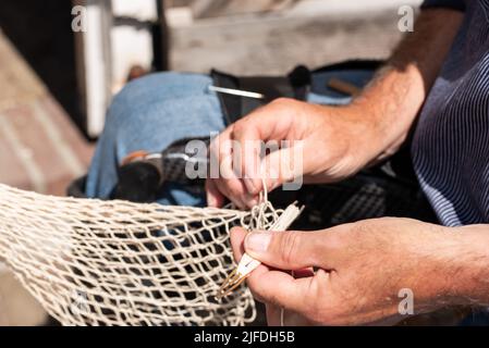 Enkhuizen, Niederlande. Juni 2022. Die Hände eines Fischers, der Fischernetze mit Nadel und Faden repariert. Hochwertige Fotos. Nahaufnahme. Stockfoto