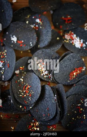 Schwarze Lebensmittel. Schwarze Chips mit Gewürzen auf einem Teller. Schwarzfood-Trend. Tintenfisch Tinte Nahrung. Stockfoto