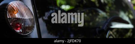 Rücklicht eines Autos mit der gesamten Heckscheibe auf der rechten Seite mit verschwommenen Reflexen von Laub. Konzentrieren Sie sich auf den linken Teil der Rückleuchte. Breitbild Stockfoto