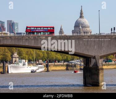 London, Großbritannien - 20. 2022. April: London Bus fährt über die Waterloo Bridge mit der St. Pauls Cathedral im Hintergrund und HQS Wellington auf dem River T Stockfoto