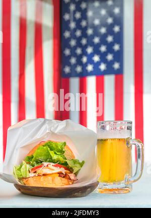 Ein Pint Lagerbier mit einem Sasebo-Burger, zubereitet mit knusprigem Speck, Tomaten und Salat in Sesambrötchen, serviert auf einem Holzteller gegen nationale Gerichte Stockfoto