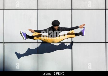 Junger erwachsener afroamerikanischer Mann, der auf eine Wand springt. Tänzerin, die Akrobatik in der Luft macht. Origineller Look, 90er-Jahre-Ästhetik. Urbane Lebensart. Platz für tex Stockfoto