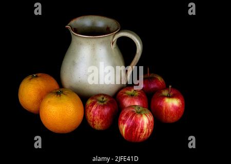 Steingutkrug mit Äpfeln und Orangen isoliert auf schwarzem Hintergrund Stockfoto