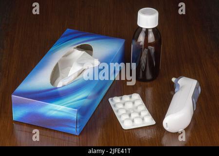 Medikamentenflasche mit Schachtel mit Taschenthermometer und Tabletten auf einer polierten Tischoberfläche Stockfoto