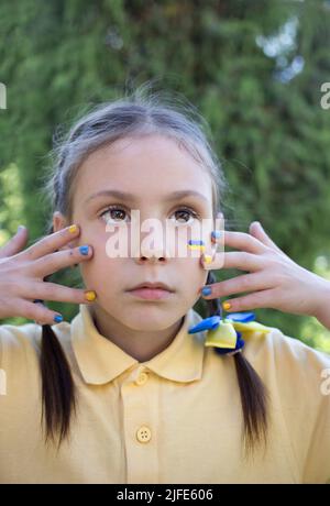 Nahaufnahme des Mädchens mit der Flagge der Ukraine auf der Wange und den gelben und blauen Nägeln. Kinder der Ukraine bitten um ein Ende des Krieges. Russische Invasion Stockfoto