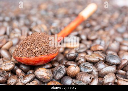 Geröstete Kaffeebohnen und Kaffeepulver oder gemahlener Kaffee in Holzlöffel isoliert auf dunklem Hintergrund. Stockfoto