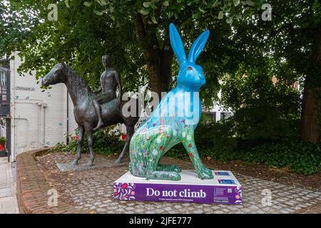 Hares of Hampshire Art Trail im Stadtzentrum von Winchester im Sommer 2022, England, Großbritannien. Bunte Hase Skulptur neben der Pferd und Reiter Statue. Stockfoto