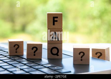 FAQ-Wort auf Holzblock auf dem Laptop mit unscharfem Naturhintergrund. Stockfoto