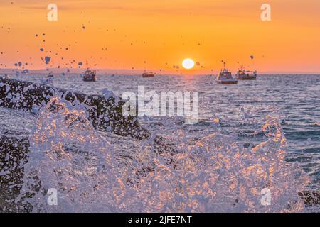 Selsey Sonnenaufgang zwischen den Fischerbooten mit beleuchteten Spray trifft das Ufer Stockfoto