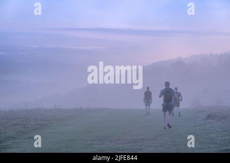 Jogger am frühen Morgen auf dem Harting Hill in den South Downs verschwinden im Nebel, wenn die Sonne zu Beginn eines neuen Tages aufgeht. Stockfoto