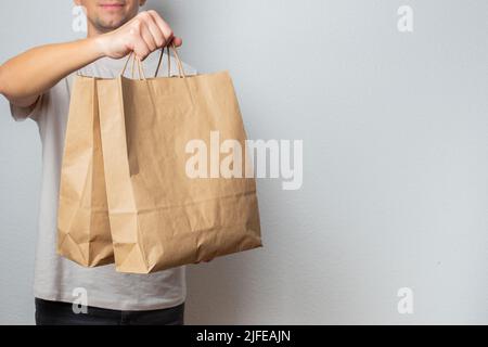 Lieferkonzept - schöner kaukasischer Liefermann, der eine Packtasche mit Lebensmitteln und Getränken aus dem Laden trägt. Isoliert auf grauem Studiohintergrund. Kopieren Stockfoto