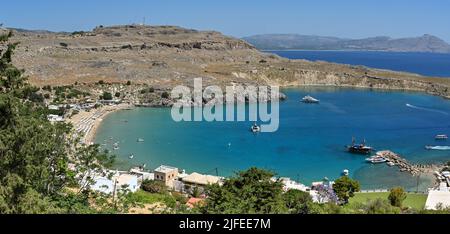 Lindos, Rhodos, Griechenland - Mai 2022: Luftaufnahme des Strandes mit Reihen von Sonnenschirmen und kleinen Booten im Meer Stockfoto