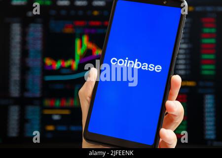 Ukraine, Odessa - Oktober, 9 2021: Hand hält Handy mit Coinbase App läuft auf Smartphone-Bildschirm mit Trading-Seite im Hintergrund. Coinbase amerikanische Kryptowährungs- und Handelsplattform Stockfoto