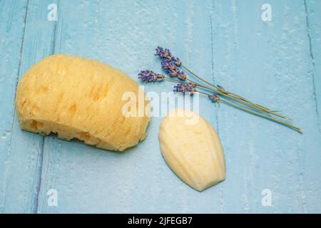 Badeball in Muschelform, Lavendelblüten und Badeschwamm als Zutaten für ein entspannendes Bad auf rustikalem Holzhintergrund Stockfoto