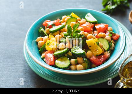 Kichererbensalat mit Tomaten, Gurke, Petersilie, Zwiebeln auf einem Teller, selektiver Fokus. Gesunde vegetarische Küche, orientalische und mediterrane Küche. Chic Stockfoto