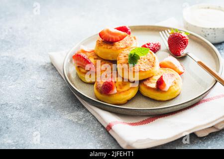 Quark-Pfannkuchen, Ricotta-Fritten oder Syrniki mit Minze und Erdbeeren. Gesundes und leckeres Frühstück am Morgen Stockfoto