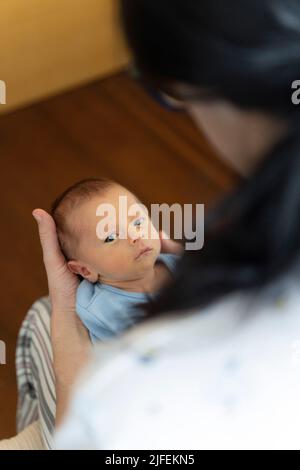 Kleines Neugeborenes, das in die Kamera schaut, während es von einer jungen Frau gehalten wird Stockfoto