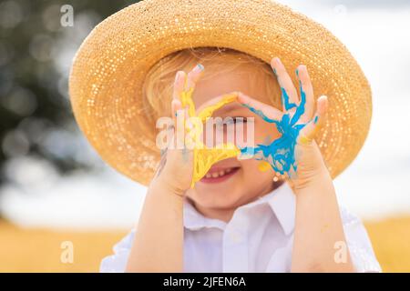 Beenden Sie den Krieg in der Ukraine. Das Konzept der Ukraine gefällt mir sehr gut. Ukrainischer Junge mit ukrainischer Flagge - gelb und blau auf den Händen gemalt, steht gegen Krieg. Stockfoto