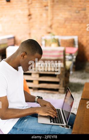 Konzentriert und verwirrt multirassischen Geschäftsmann sitzen auf Bank mit Laptop im Straßencafe, lesen snd notieren Daten Stockfoto