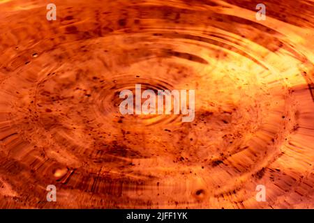 Kreise und kleine Wellen auf orange-brauner Flüssigkeit. Hintergrund Stockfoto