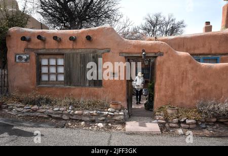 Eine Frau verlässt ein historisches lehmziegelhaus aus dem 19.. Jahrhundert in Santa Fe, New Mexico. Stockfoto