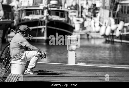 Eine Graustufenaufnahme eines Mannes, der das Meer im Hafen von Palermo beobachtet Stockfoto